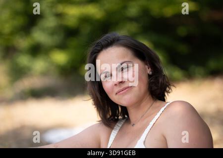 Portrait de femme brune souriante penchée légèrement en arrière sur la plage d'été, expression douce à lèvres fermées avec espace de copie Banque D'Images
