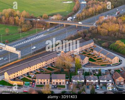 WARRINGTON, CHESHIRE, ANGLETERRE - 17 NOVEMBRE 2025 : une vue aérienne montre des maisons de ville nouvellement construites de 3 étages à côté de l'autoroute M62 Banque D'Images