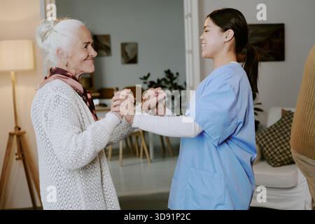 Femme âgée souriant tout en se tenant la main avec la jeune infirmière hispanique Banque D'Images