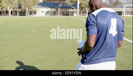 Tenant le ballon de football, joueur de football en maillot bleu numéro 4 debout sur le terrain de gazon, espace de copie Banque D'Images