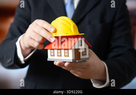 Un homme d'affaires pose un casque jaune sur une maison. Le projet de rénovation commence. La planification de la construction, la budgétisation de la réparation de la maison et l'immobilier se développent Banque D'Images
