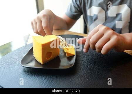 Enfant utilisant une fourchette pour manger un morceau de cheesecake jaune sur une assiette noire. Dessert sucré pour le menu enfants ou le café. Banque D'Images
