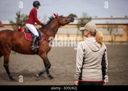 Entraîneur équestre expérimenté encadrant le jeune cavalier avec cheval lors de la séance de pratique dans le paddock avant la compétition Banque D'Images