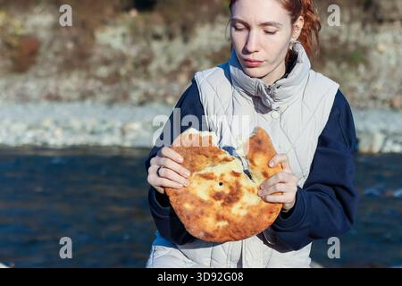 Heureuse jeune femme riant joyeusement tout en tenant deux morceaux de pain plat fraîchement déchiré dans la forêt d'automne Banque D'Images