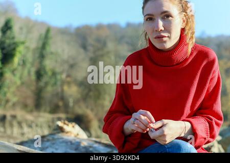 Vue de face d'une femelle rousse en col roulé tenant un petit objet à l'extérieur près des rochers et des arbres par temps clair Banque D'Images