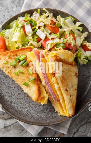 Pain grillé One-Pan oeuf avec jambon et fromage fondu Gooey servi avec une salade fraîche en gros plan sur l'assiette sur la table. Vue de dessus verticale Banque D'Images