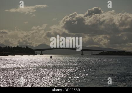 Vue rétroéclairée du pont Skye sur le Kyle de Lochalsh, en Écosse, photographiée depuis un bateau sous les nuages et le ciel dégagé. Banque D'Images