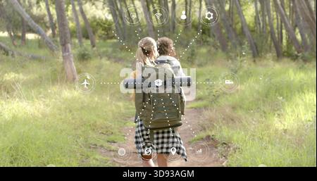 Randonneurs femmes marchant en haut jaune et jupe à carreaux sur le sentier forestier, avec des icônes AR sur le sac à dos Banque D'Images