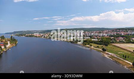 Une photographie aérienne sereine montre le canal Asparuhovo divisé par des paysages luxuriants, avec des structures de la ville bordant le front de mer sous un ciel bleu clair. V Banque D'Images