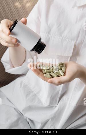 Femme versant des capsules vertes de la bouteille dans une main ouverte gros plan Banque D'Images