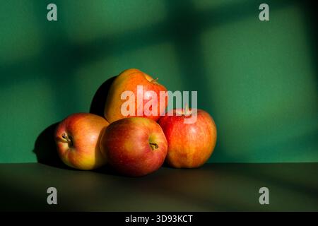 Les pommes s'empilent sur fond vert avec effet de lumière de fenêtre. Banque D'Images