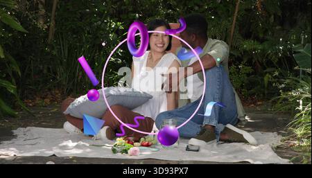 Couple assis tenant l'oreiller gris sur la couverture de pique-nique dans le jardin ombragé, recouvrement violet AR apparaissant Banque D'Images