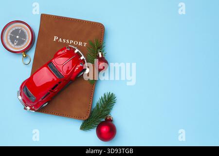 Vacances de Noël. Passeport, boussole, voiture jouet, boules et branches de sapin sur fond bleu clair, plat. Espace pour le texte Banque D'Images