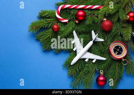 Vacances de Noël. Avion jouet, boussole, branches de sapin, boules et canne à bonbons sur fond bleu, plat. Espace pour le texte Banque D'Images