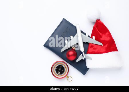 Vacances de Noël. Passeport, modèle d'avion, chapeau de Père Noël, ornement et boussole sur fond blanc, pose à plat. Espace pour le texte Banque D'Images