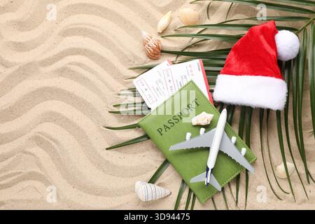Vacances de Noël. Passeport avec billets, maquette d'avion, coquillages et chapeau de Père Noël sur la plage, pose à plat. Espace pour le texte Banque D'Images