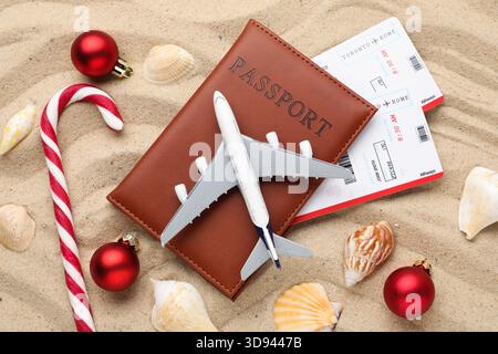 Vacances de Noël. Passeport avec billets, maquette d'avion, coquillages, canne à bonbons et ornements sur la plage, pose à plat Banque D'Images