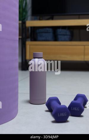 Gros plan vertical d'haltères violets et d'une bouteille d'eau sur le sol avec un arrière-plan en bois flou doux Banque D'Images