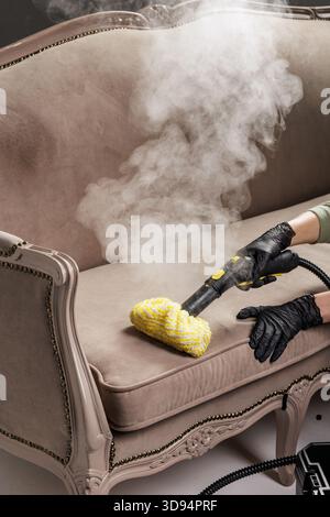Nettoyant ganté à l'aide d'une vadrouille à vapeur avec tampon jaune pour désinfecter le siège rembourré du canapé et enlever la saleté profonde et les germes Banque D'Images