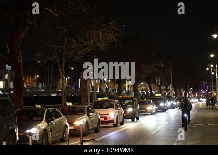 Dublin, Irlande - 03 décembre 2025 - Une file de taxis sur une route le long des quais alors que les chauffeurs de taxi de Dublin organisent une manifestation « Go slow » aux heures de pointe pour protester contre les nouveaux tarifs fixes d'Uber avec des retards dans la circulation dans la capitale irlandaise Banque D'Images