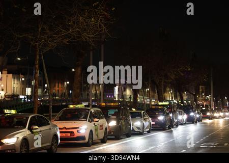 Dublin, Irlande - 03 décembre 2025 - Une file de taxis sur une route le long des quais alors que les chauffeurs de taxi de Dublin organisent une manifestation « Go slow » aux heures de pointe pour protester contre les nouveaux tarifs fixes d'Uber avec des retards dans la circulation dans la capitale irlandaise Banque D'Images