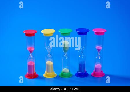 Sabliers en verre transparent avec du sable coloré sur fond bleu comme symbole du temps. Mise au point sélective Banque D'Images