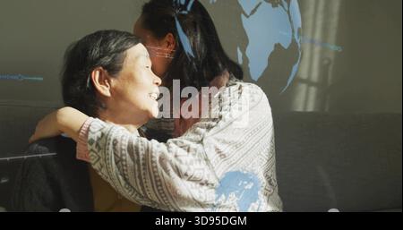 Embrassant sa fille dans un pull à motifs sur un canapé gris à la maison tandis que la projection de carte bleue couvre le mur Banque D'Images