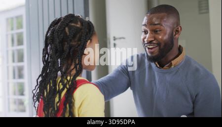 Saluant l'homme en pull bleu atteignant vers la fille en haut jaune à l'entrée de la maison, sac à dos rouge Banque D'Images