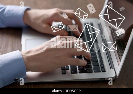 Homme envoyant ou recevant des e-mails sur ordinateur portable à table, gros plan. Lettres qui volent hors de l'écran Banque D'Images