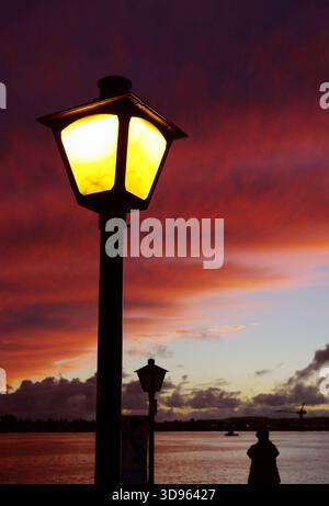 Paysage crépusculaire spectaculaire. Un lampadaire lumineux se dresse contre le ciel du coucher de soleil ardent, illuminant la scène. Une figure solitaire apprécie la beauté. Banque D'Images
