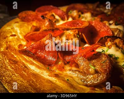 Gros plan d'une pizza au pepperoni fraîchement cuite avec une croûte dorée, du fromage mozzarella fondu et des tranches de pepperoni salées, garnies d'herbes fo Banque D'Images