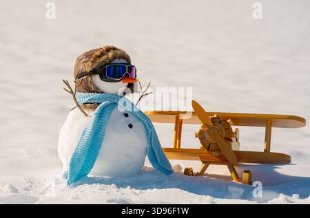 Pilote bonhomme de neige dans la neige. Livraison d'hiver avec bonhomme de neige. Pilote bonhomme de neige carte postale de Noël. Aviateur bonhomme de neige avec avion en bois. Bonhomme de neige décoré pour Banque D'Images