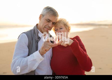 Couple senior partageant l'amour faire le coeur de la main sur la plage Banque D'Images