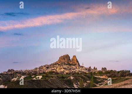 Vue aérienne des anciennes formations rocheuses et des habitations du château d'Uchisar brille sous les teintes douces et pastel du ciel crépusculaire, Goreme, Cappadoce, T. Banque D'Images