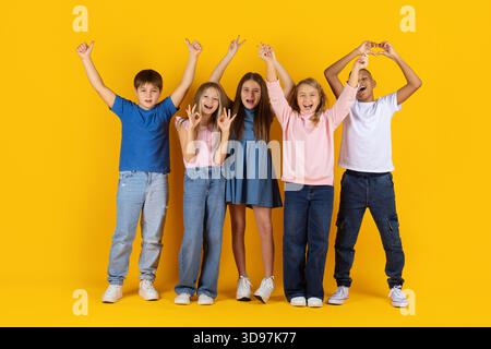 Groupe joyeux d'enfants préadolescents levant la main et faisant des gestes ludiques Banque D'Images