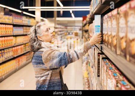 Femme senior faisant des courses, cherchant un produit sur une étagère dans un supermarché bien éclairé Banque D'Images