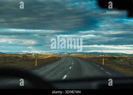 Vue depuis la voiture conduisant sur une route rurale courbe parmi les prairies et le champ de lave dans la journée couverte à Islande Banque D'Images
