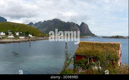 Maison rouge traditionnelle avec un toit vert donnant sur un fjord paisible. Reine lofoten, îles norvège Banque D'Images