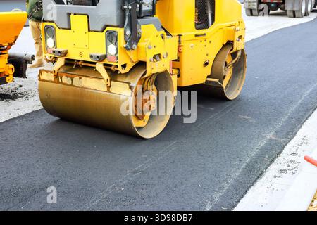 Rouleau lourd compresse l'asphalte fraîchement posé sur la route en construction pendant Banque D'Images