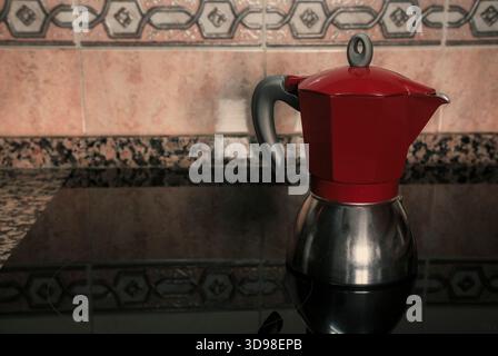 Belle cafetière moka rouge préparant du café sur une plaque vitrocéramique. Design intérieur de cuisine maison avec espace de copie. Banque D'Images