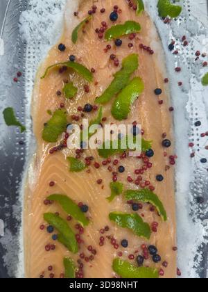 Gros plan de saumon mariné avec du zeste de citron vert, des grains de poivre rose et de la vodka dans une cuisine professionnelle Banque D'Images
