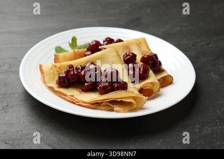 Crêpes savoureuses aux cerises et à la menthe sur table noire, gros plan Banque D'Images