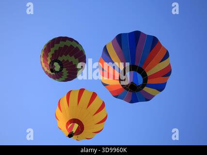 Trois montgolfières colorées en vol, vues d'en bas, contre le ciel bleu clair, Gualdo Cattaneo, Pérouse, Ombrie, Italie Banque D'Images