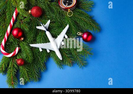 Vacances de Noël. Avion jouet, boussole, branches de sapin, boules et canne à bonbons sur fond bleu, plat. Espace pour le texte Banque D'Images