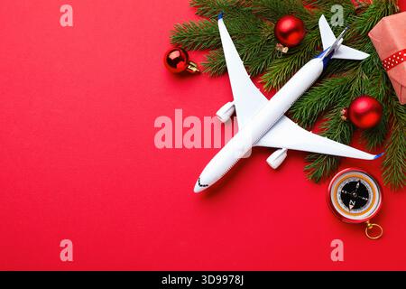 Vacances de Noël. Avion jouet, boussole, boîte cadeau et décor sur fond rouge, pose plate. Espace pour le texte Banque D'Images