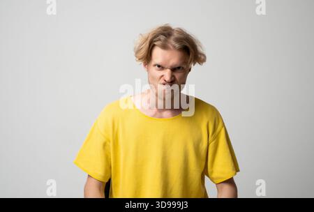 Jeune homme en colère regardant en avant avec une expression tendue et un visage sillonné dans un portrait de studio neutre lumineux Banque D'Images