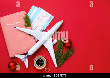 Vacances de Noël. Passeport avec billets, avion jouet, boussole, branches de sapin et boules sur fond rouge, pose à plat. Espace pour le texte Banque D'Images