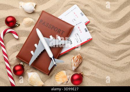 Vacances de Noël. Passeport avec billets, maquette d'avion, coquillages, canne à bonbons et ornements sur la plage, pose à plat Banque D'Images