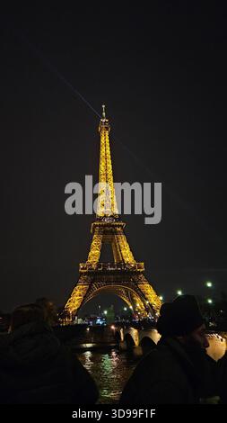 Tour Eiffel brillante la nuit à Paris, France, avec des reflets sur le trottoir humide et la foule animée. Banque D'Images
