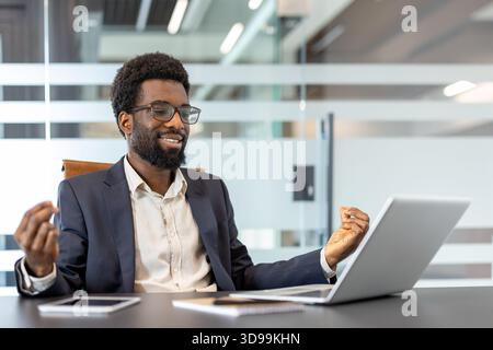 Jeune homme d'affaires méditant en position de lotus tout en étant assis au bureau à l'intérieur du bureau. Homme parcourant des cours de formation de méditation en ligne à l'aide d'un ordinateur portable. Banque D'Images